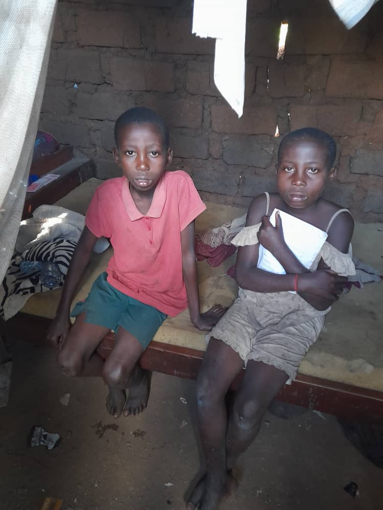 Two children sitting on a bed in a mud-brick home in Buseesa